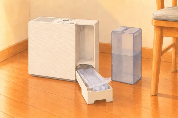 タンクを外した加湿器の、右側の空いた所の下から、トレイを前へ引き出したところ。トレイの中に、トレイの形をした半透明の薄い使い捨てのカバーが敷いてあり、端が少し持ち上がっている。外したタンクが横に立っている